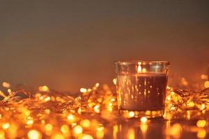 Burning candle with a golden garland lights in bokeh on dark background photo