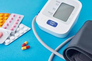 monitor de presión arterial digital y píldoras médicas sobre un fondo azul. foto