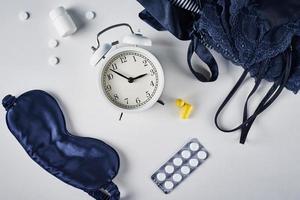 Alarm clock, sleeping mask, ear plugs and pills on a white background, top view photo