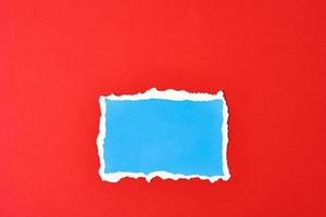 Ripped blue paper torn edge sheet on a red background photo