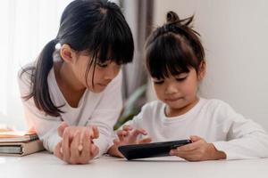 Concept kids and gadgets. Two little girls siblings sisters look at the phone and smile. They hold a smartphone watch videos, learn, play games, speak online. Internet for children. Parental control photo