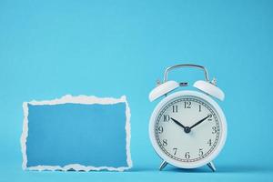 Alarm clock with bells and empty torn paper sheet on the blue background photo