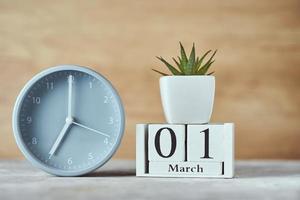 Alarm clock with wooden block calendar date 1st march and plant on the table photo