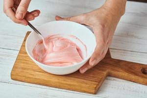 Woman whisking red cream for decorating cookies in a bowl on kitchen, closeup photo