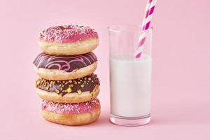 Stack of colorful donuts decorated and glass of milk on a pink background photo