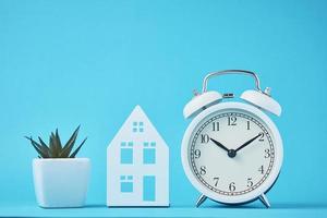 White retro alarm clock and miniature house on the blue backgroumd photo