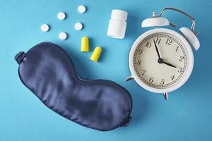 Alarm clock, sleeping mask, ear plugs and pills on a blue background, top view photo