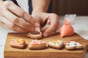 Woman hand decorate cookies in shape of heart, closeup photo