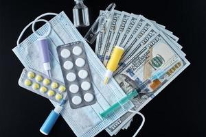 Pills, protective mask, medical items and dollar bills on dark background. photo