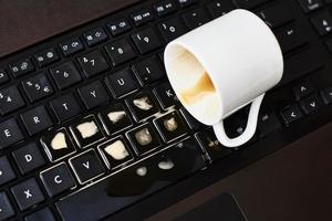 derrame café de una taza blanca en el teclado de la computadora portátil foto