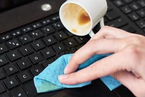 Hand cleans spilled coffee on laptop keyboard with a rag photo