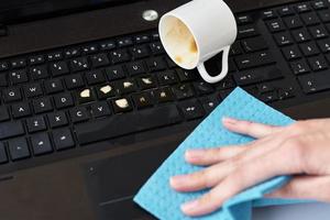 Hand cleans spilled coffee on laptop keyboard with a rag photo