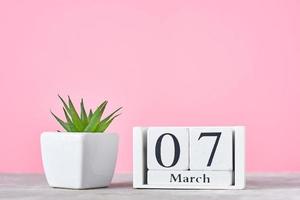 Wooden block calendar with date 7 march and plant on the pink background photo