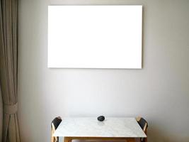 An empty canvas picture frame hanging on the wall, light brown fabric curtain, wooden table with Marble top, two wooden chairs, an avocado fruit on the table with clipping path photo