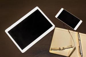 Office table, mobile phone, tablet, glasses, notebook and pen with copy space. Gadgets on a wooden table.  Top view photo