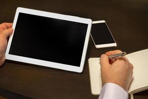 Work place, a businessman writes information from a tablet to the notebook photo