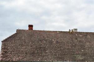 The old ancient sloping triangular roof of the house, the cottage is dirty with tusks overgrown with moss against the blue sky photo