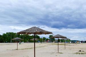 An empty deserted beach in bad weather, cold autumn in the off-season with thatched sun umbrellas against the blue sky photo