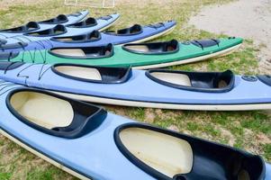 A lot of blue and green canoe kayaks with front parts of the noses for water sports, swimming lie on the beach on the beach photo