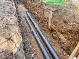 laying of underground communications for residential buildings. plumbing pipes of black color are buried deep in an earthen ditch photo