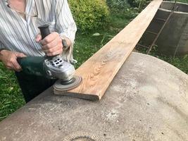 The man works with his hands, grinds the disk around for the grinder, the electric tool for grinding and polishing the surface of the wooden board photo