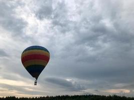 Large multi-colored bright round rainbow colored striped striped flying balloon with a basket against the sky in the evening photo