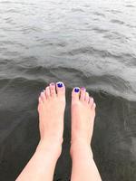 hermosos pies femeninos de los pies con dedos con una manicura de moda multicolor se dejan caer colgando en agua fría y oscura foto