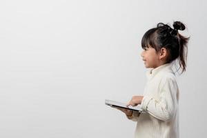 Asian little girl holding and using the digital tablet on white studio background, free copy space photo