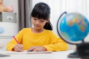 Asian schoolgirl doing her homework with digital tablet at home. Children use gadgets to study. Education and distance learning for kids. Homeschooling during quarantine. Stay at home photo