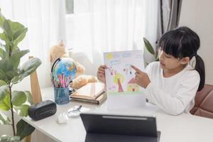 niña asiática tomando clases en línea y feliz por el concepto de pandemia de coranavirus en cuarentena en la escuela en casa foto