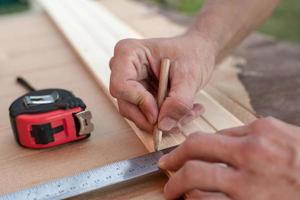 Carpenter hands take measurements with a metal ruler on a wooden board and mark the required length with a pencil. photo