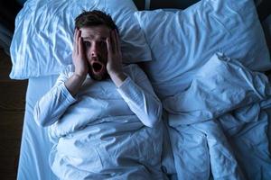 el hombre tuvo una terrible pesadilla, se despertó horrorizado, mirando asustado con grandes ojos a la cámara. concepto de insomnio y salud mental. foto