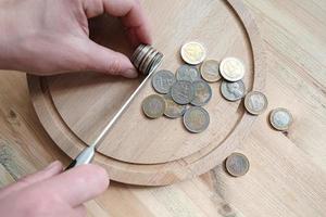 Hands cut a stack of euro and dollar coins with a knife, separating them like pieces of food on a cutting board. Concept of taxes, fraud or profit. photo