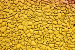 Wall of small stones painted yellow. Bright textured background. Copy space. photo