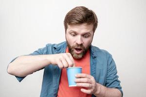 un hombre sorprendido con un vaso de papel en la mano saca algo del té recién bebido con sorpresa. concepto de productos de mala calidad. foto