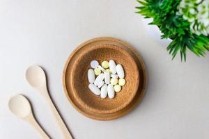 A handful of pills in a wooden plate with spoons and green plant. The concept of medcine, treatment. Top view. photo