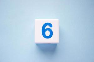 Close-up photo of a white plastic cube with a blue number 6 on a blue background. Object in the center of the photo