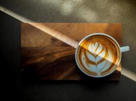 A cup of hot latte with beautiful art on top with nature light on a wood serve on a table photo