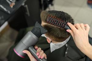 un adolescente se corta el pelo durante una pandemia en la barbería, se corta el pelo y se seca el pelo después de un corte de pelo. foto