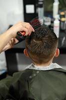 un adolescente se corta el pelo durante una pandemia en la barbería, se corta el pelo y se seca el pelo después de un corte de pelo. foto