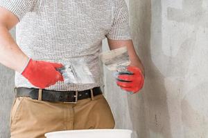 A man with a small spatula applies lime plaster on a large spatula, lime plaster on the walls and ceiling. photo