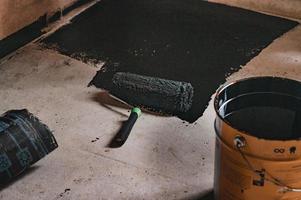 Aplicación de resina caliente al piso para impermeabilización, rodillo y balde de resina. foto