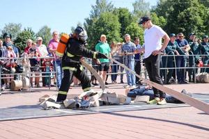 A fireman in a fireproof suit and a helmet running with an oxygen balloon pulling, holding a fire hose at a fire sport competition. Minsk, Belarus, 08.07.2018 photo