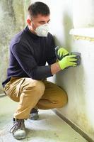 Fungus and mold is a manifestation of excess moisture in the room, a man with a spatula removes fungus and mold from the wall. photo