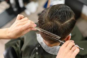 un adolescente se corta el pelo durante una pandemia en la barbería, se corta el pelo y se seca el pelo después de un corte de pelo. foto