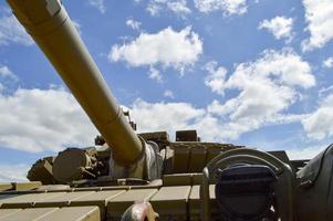 A large green military metal armored deadly dangerous iron Russian Syrian battle tank with a gun turret and a goose is parked parked against a blue sky and clouds outside the city photo