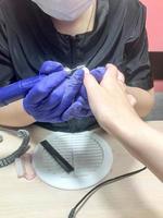 la mujer, la niña, el maestro de la manicura, un servicio de uñas hace una manicura con guantes azul oscuro en las manos, el dispositivo, una lima para las uñas foto