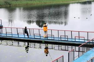 gente, hombres están pescando desde el pontón, delantal, puente en el lago con patos en el centro de recreación, sanatorios en otoño foto