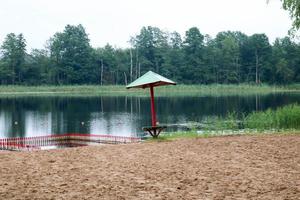 A lone, sagging sunken umbrella and fencing, a playpen for bathing children on a sandy beach on the shore of a lake, a river at a recreation center, a sanatorium in the fall on a cloudy day photo