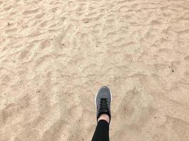 el pie en el zapato de bota gris da un paso contra el fondo de una hermosa arena cálida de playa dorada amarilla suelta natural foto